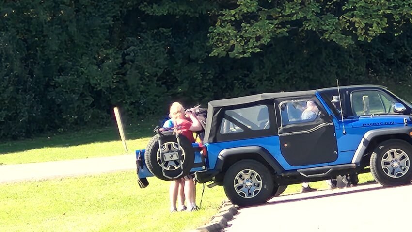 People loading a blue Jeep at a park on a sunny day